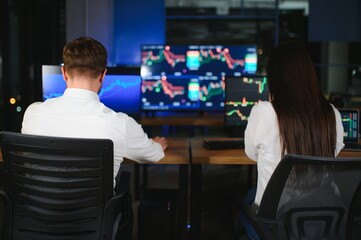 Team of stockbrokers are having a conversation in a dark office with display screens