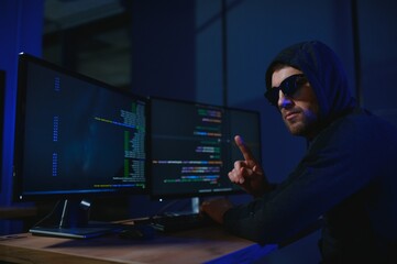 hacker sitting at desk in dark atmosphere. A computer programmer or hacker. Anonymous computer hacker.