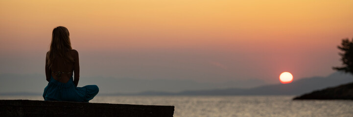 Young woman sitting on a pier by the sea at sunrise