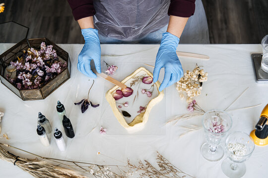 Hands arranging pressed flowers into resin frame, showcasing traditional crafts in modern DIY home decor. Eco-friendly, sustainable crafting techniques.