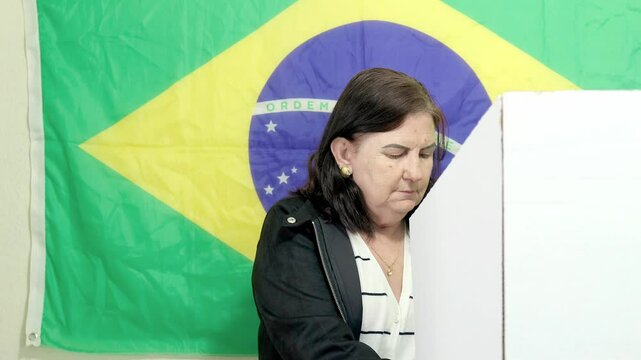 Eleitora mulher brasileira na cabine de vota&ccedil;&atilde;o escolhendo o seu candidato na urna eletr&ocirc;nica brasileira. Elei&ccedil;&otilde;es presidenciais e municipais no Brasil. No fundo, a bandeira do Brasil decora o local.