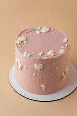 Beautiful birthday cake with peach color chocolate icing on the beige pastel background decorated with cream flowers