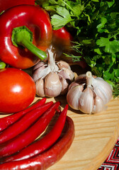 Pepper, tomatoes, garlic and greens on a wooden board. Set of vegetables for adjika.