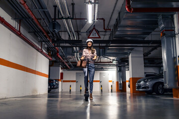 Fototapeta premium Portrait of confident woman with helmet riding electric scooter in underground garage.
