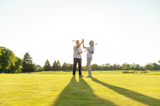 elderly senior couple in uniform celebrating victory and success in golf game and giving high five, old man and woman playing golf on golf course at sunset and doing outdoor sports
