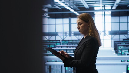Computer scientist doing checkup, inputting data on tablet of needed fixes in server hub. Woman...