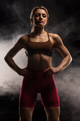 Strong woman in athletic wear posing confidently in a studio against a smoky background, embodying strength and empowerment in sports and fitness photography