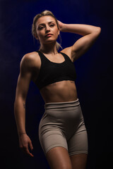 Obraz premium Confident athletic woman in sportswear posing with hand on head against dark background, exuding strength and empowerment