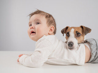 Cute baby boy and Jack Russell terrier dog lying in an embrace on a white background. 