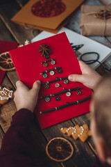 Concept of Christmas craft, handmade presents, family leisure time, hobby, recreation. Flat lay, top view with paper postcard with new year fir tree made with buttons, branches. Gingerbread cookies