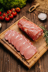Raw pork loin with rosemary and fresh tomatoes on cutting board, perfect for culinary presentations