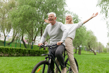 elderly senior couple riding bicycle in park and having fun, old man and woman actively relaxing together outdoors, freedom concept