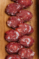 Close-up of thinly sliced salami on a wooden board, showcasing rich marbling and gourmet quality