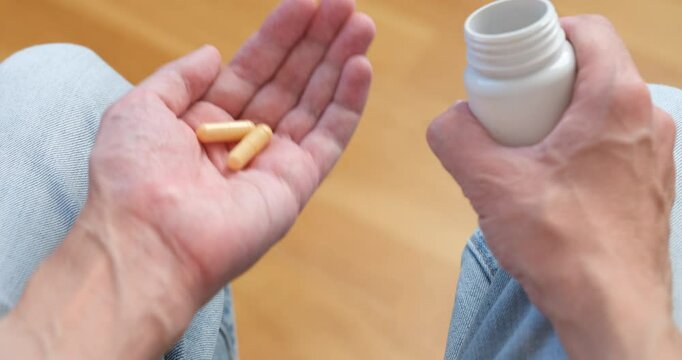 A man pouring vitamin B complex pills from a plastic bottle into his palm and taking them.