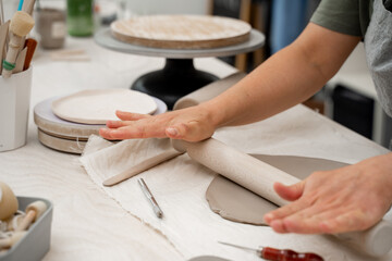 Rolling wooden stick to make flat sheet of clay. Preparing clay for cutting and assembling it. Slab building method in ceramics crafting.