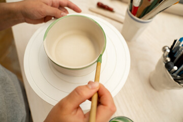Girl is making a colorful decoration of a clay project with paint and water. Painting ceramic products using acrylic paint and brush.