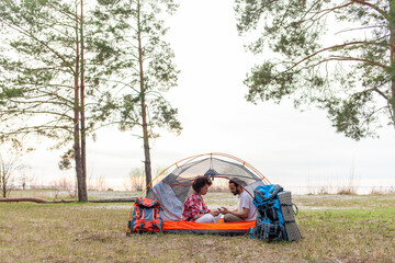 young african american couple tourists with camping equipment and backpacks sitting in tent in forest and using smartphone, man and woman camping relaxing and watching mobile online