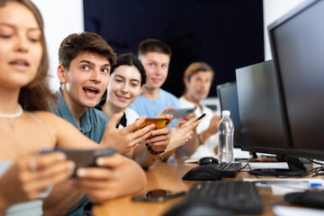 Excited young developer working at IT startup, watching project presentation with team gathered around table and using mobile phones for real-time data sharing