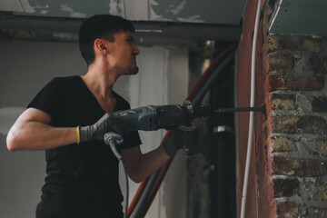 A young man breaks a wall with a perforator.