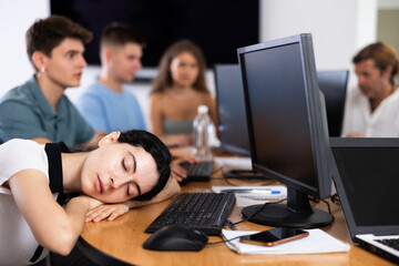 Fototapeta premium Exhausted students find solace in sleep, their heads resting on lecture hall desks during break.