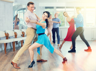 Portrait of positive adult pairs of different ages enjoying tango in modern dance hall together