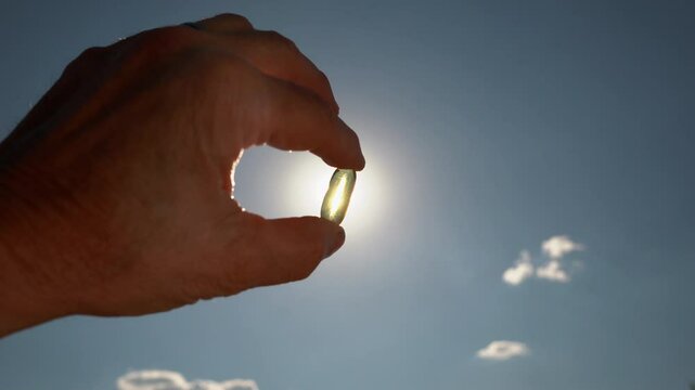 A man holding a vitamin D capsule in the sunlight