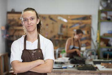 Guy working in carpentry workshop with female colleague. He make decorative objects products,...