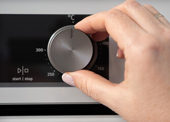 Woman adjusting modern white oven in kitchen.  Female hand pushing and turning knobs on oven...