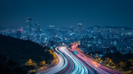 Obraz premium Night cityscape with light trails on highway, high buildings illuminated in background, in a bustling urban area.