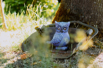 Purple owl statue resting by a tree in a garden, with soft sunlight filtering through leaves
