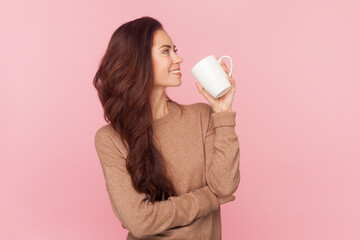Side view portrait of joyful smiling woman with wavy hair drinking coffee or tea in morning looking...