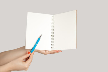 Closeup of woman hand showing open notebook with empty pages, pointing at something with pen, copy space. Indoor studio shot isolated on gray background.