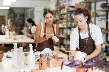 Fototapeta premium During lesson, guy levels surface of ceramic plate, processes it with spatula, prepares product before decorating and painting. Hand made art, hobbies and creativity.
