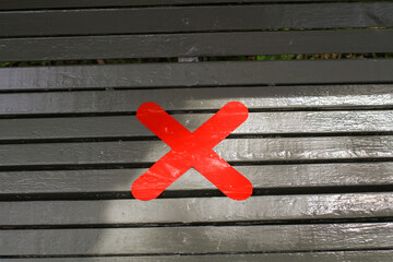 Red cross on wooden bench under sunlight in public park. Safe Seating. Prohibit people from sitting...