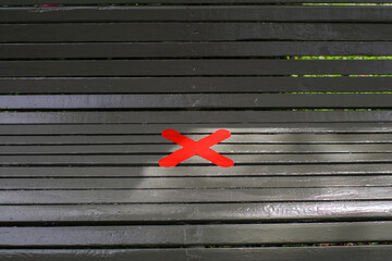 Red cross on wooden bench under sunlight in public park. Safe Seating. Prohibit people from sitting...