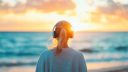 A woman with headphones relaxes as she watches the vibrant sunset over the ocean waves, embracing the tranquil moment