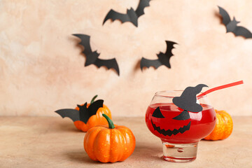 Glass of delicious red cocktail for Halloween with pumpkins and paper decor on beige background,...
