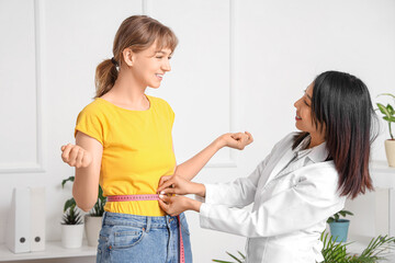 Female Asian nutritionist measuring patient's waist in office