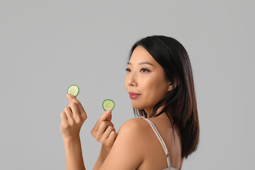 Beautiful Asian woman with cucumber slices on grey background