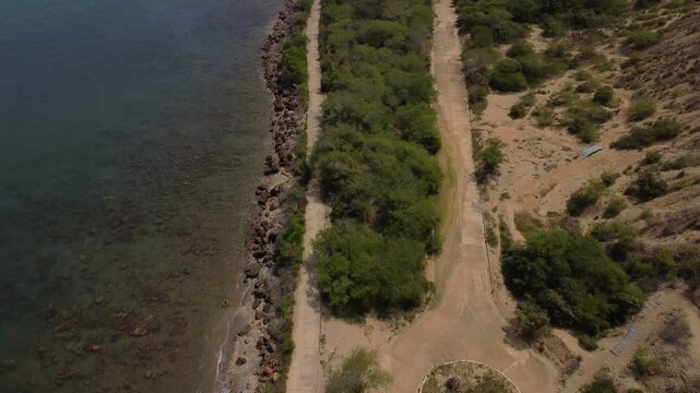 Aerial tracking by drone of a compact blue car, rolling on the ridge of a mountain, with arid vegetation and beach in the background