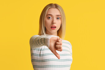 Upset young woman showing dislike on yellow background