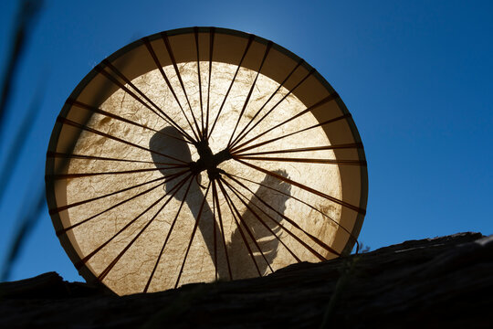 A silhouette image of a handmade leather meditation drum with sacred feather against a bright blue sky. 
