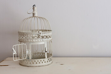 A clean and simple image of a retro metal bird cage on a vintage desk top.