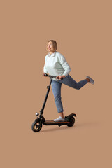 Beautiful mature woman with kick scooter and headphones on beige background