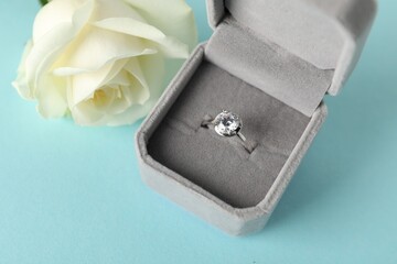 Beautiful ring with gemstone in box and flower on light blue background, above view