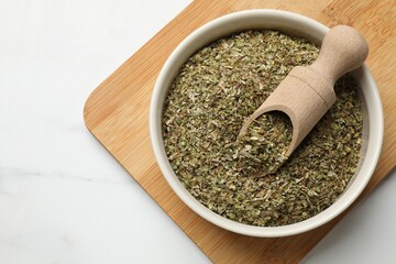 Dried oregano in bowl and scoop on white marble table, top view