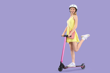 Beautiful young woman in helmet riding modern electric kick scooter on lilac background