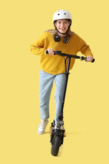 Beautiful young woman in helmet riding modern electric kick scooter on yellow background © Pixel-Shot