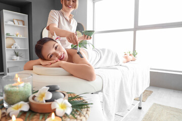 Massage therapist applying mud on young woman's back in spa salon