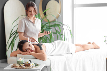 Massage therapist applying mud on young woman's back in spa salon